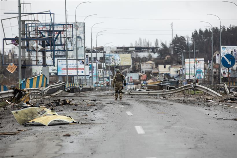 02.04.2022, Ukraine, Butscha: Ein ukrainischer Soldat geht entlang von Leichen auf einer zerstörten Straße.
