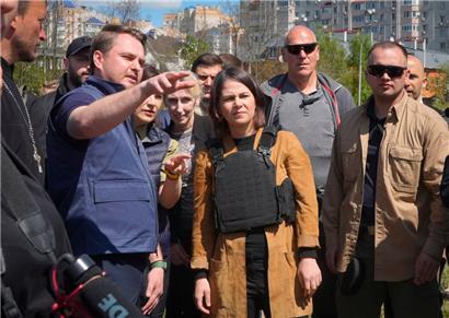 10.05.2022, Ukraine, Butscha: Außenministerin Annalena Baerbock (Bündnis 90/Grüne) hört einem ukrainischen Kriegsstaatsanwalt zu während ihres Besuchs in der Nähe eines Massengrabes in Butscha
