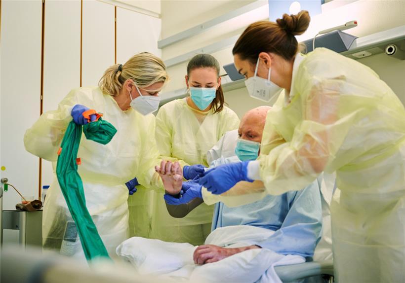 30.11.2022, Berlin: Beatrice Bosse (l-r), Medizinproduktberaterin im Bereich Narbentherapie, Julia Huk, ukrainische Rehabilitationärztin, und Jenny Dornberger (r), Oberärztin im Zentrum für Schwerbrandverletzte mit Plastischer Chirurgie, stehen während der Visite im Unfallkrankenhaus Berlin um einen Soldaten aus der Ukraine, der Brandverletzungen erlitten hat 
