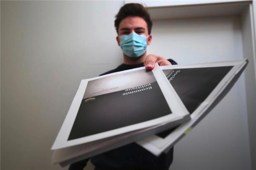 Abschlussschüler Michel Rigo hat die Maske an und zeigt die Lernbücher seines Hauptfaches „Economie politique“
