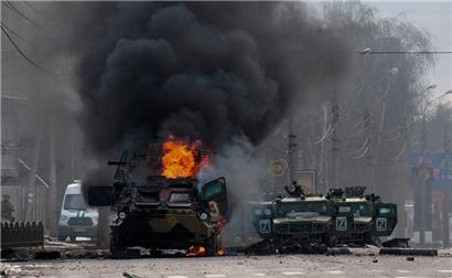 Am Sonntag in Charkiw: Ein gepanzerter Mannschaftswagen brennt und beschädigte Nutzfahrzeuge stehen nach Kämpfen in Charkiw auf einer Straße
