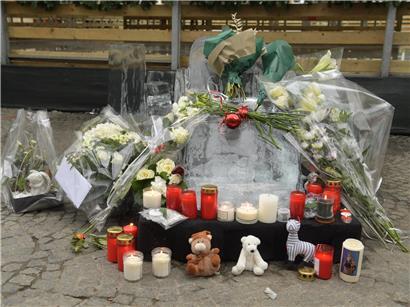 Blumen, Kerzen und Stofftiere an den Überresten einer geschmolzenen Eisfigur als Gedenkstätte nach Unglück