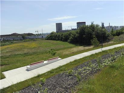 Sitzgelegenheiten im sonnigen Park Belval mit grünen Bäumen und klar blauem Himmel