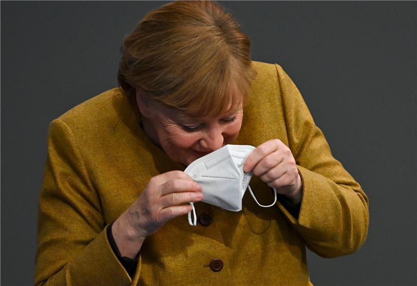 Angela Merkel lacht sich in die Maske, nachdem sie selbige auf dem Rednerpult im Bundestag vergessen hatte
