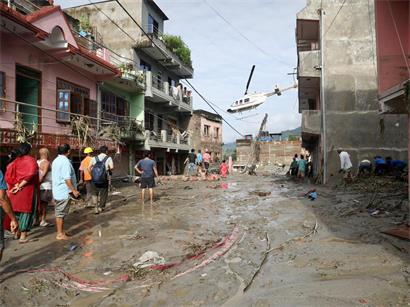 Anwohner beobachten, wie ein Hubschrauber über Häuser fliegt, die nach Sturzfluten in Devighat in der Gemeinde Bidur im nepalesischen Distrikt Nuwakot unter Schlamm begraben sind