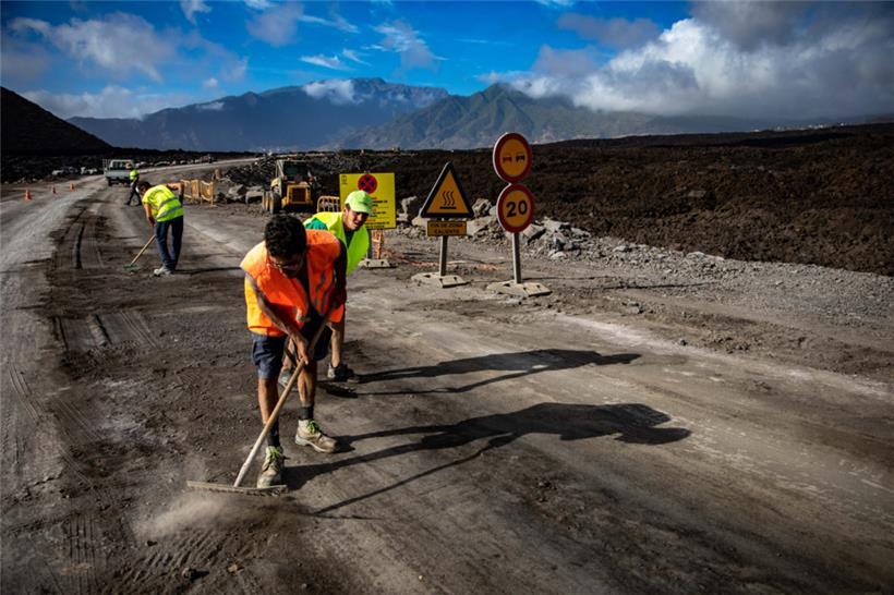 Arbeiter sind am 12. September 2022 auf der Kanareninsel La Palma an einer mit Lava bedeckten Straße im Einsatz. Durch den Plan „Recupera La Palma“ (Palma zurückgewinnen) sollen die Verbindungen zwischen dem Norden und dem Süden der Insel wiederhergestellt werden. Die Lavaströme hatten wichtige Straßen blockiert. 
