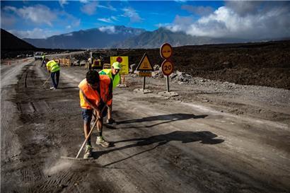 Arbeiter sind am 12. September 2022 auf der Kanareninsel La Palma an einer mit Lava bedeckten Straße im Einsatz. Durch den Plan „Recupera La Palma“ (Palma zurückgewinnen) sollen die Verbindungen zwischen dem Norden und dem Süden der Insel wiederhergestellt werden. Die Lavaströme hatten wichtige Straßen blockiert. 
