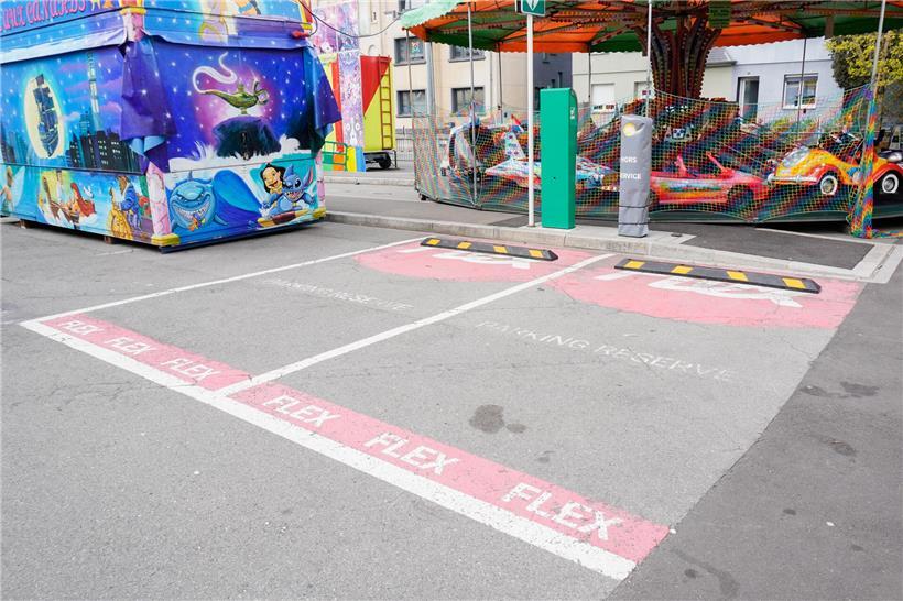 Schausteller an eingeschränkter E-Auto Ladestation auf Jahrmarkt mit Elektrofahrzeugen im Hintergrund