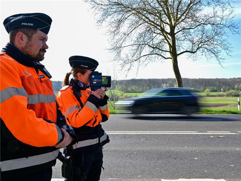 Polizeibeamte bei Geschwindigkeitskontrolle mit Messgerät an Straße, 300 Bußgeldbescheide bei 288 Kontrollen