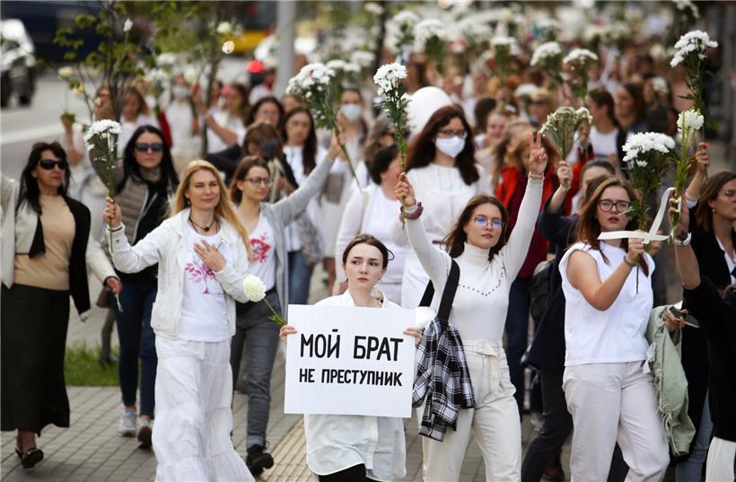 Belarussische Frauen, von denen eine ein Plakat mit der Aufschrift „Mein Bruder ist kein Krimineller“ hält, recken bei einem Protest weiße Blumensträuße in die Luft, um ihre Solidarität mit Demonstranten auszudrücken
