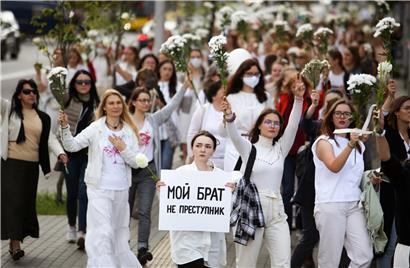 Belarussische Frauen, von denen eine ein Plakat mit der Aufschrift „Mein Bruder ist kein Krimineller“ hält, recken bei einem Protest weiße Blumensträuße in die Luft, um ihre Solidarität mit Demonstranten auszudrücken
