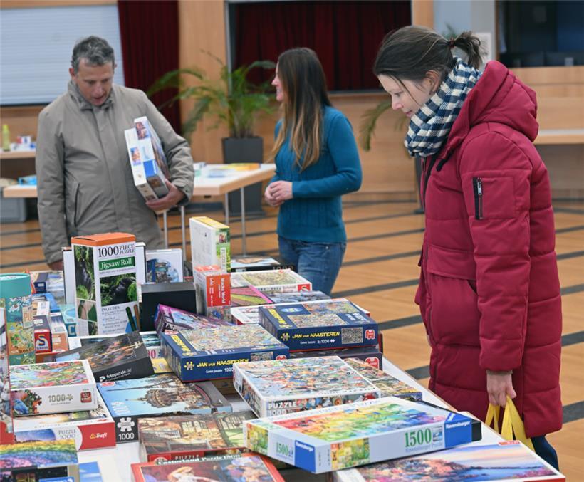 Besucher der Puzzle-Tauschbörse stöbern konzentriert an einem der Tische voller Puzzles und suchen nach ihrem nächsten Lieblingsmotiv
