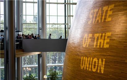 Besucher gehen über eine Brücke in den sogenannten „Hémicycle“, den Kern des Europäischen Parlaments in Straßburg, während dieser von außen mit dem Schriftzug „State of the Union“ angestrahlt wird
