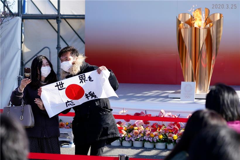 Besucher stehen mit einer japanischen Nationalflagge samt Schriftzeichen, welche soviel wie «Die Welt unterstützen» bedeuten, in der Nähe der Olympischen Flamme während der «Flame of Recovery-Tour» der Olympischen Spiele.
