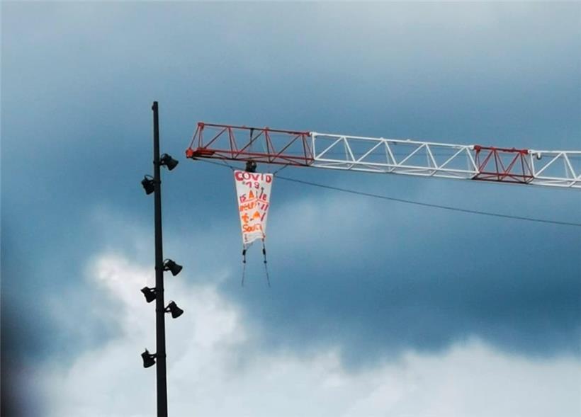 Mann klettert auf Kran und rollt Protestbanner aus 