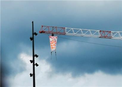 Mann klettert auf Kran und rollt Protestbanner aus