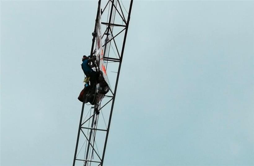 Mann klettert auf Kran und rollt Protestbanner aus 
