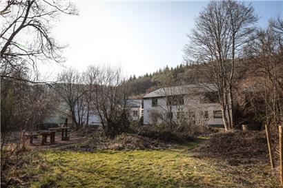 Blick in den Garten: Die über 200 Jahre alte Mühle (Gebäude im Hintergrund) ist seit 1997 im Besitz von „natur & ëmwelt – Fondation Hëllef fir d’Natur“. Seit 2005 wurden die Gebäude mit Hilfe europäischer Gelder renoviert. So ist ein Wassererlebniszentrum (WEZ), die Muschelzuchtstation für Süßwassermuscheln und der Natura 2000 Saal für Workshops und Vorträge…
