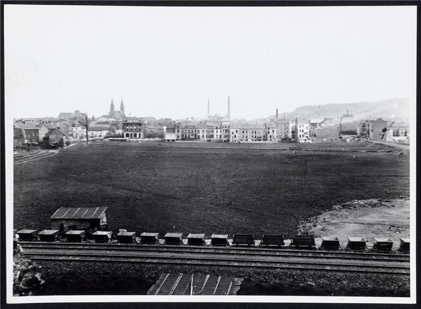 Blick auf den Brill, eine sumpfige Wiese, zwischen Kanalstraße (damals Redinger Straße) und der im Bau befindlichen Alzettestraße (damals Poststraße) und auf die Häuserreihe der Wiesenstraße (heute rue du X Septembre). Links zieht die Alzette entlang der Escher Wiesen und Straßen. Im Hintergrund Josephskirche, Industrie- und Handelsschule und Metzeschmelz. Vorne die Lefèvre-Privatbahn. Foto um 1910. 
