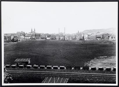 Blick auf den Brill, eine sumpfige Wiese, zwischen Kanalstraße (damals Redinger Straße) und der im Bau befindlichen Alzettestraße (damals Poststraße) und auf die Häuserreihe der Wiesenstraße (heute rue du X Septembre). Links zieht die Alzette entlang der Escher Wiesen und Straßen. Im Hintergrund Josephskirche, Industrie- und Handelsschule und Metzeschmelz. Vorne die Lefèvre-Privatbahn. Foto um 1910. 
