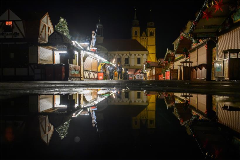 Buden des Weihnachtsmarktes, das Rathaus und die Johanniskirche spiegeln sich in einer Regenpfütze
