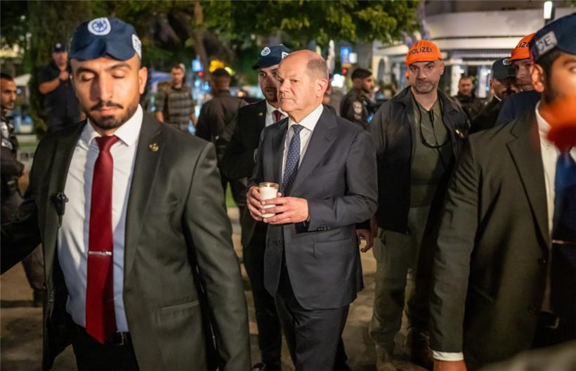 Bundeskanzler Olaf Scholz (SPD) steht, umringt von Bodyguards, bei seinem Solidaritätsbesuch in Israel mit einer Kerze in der Hand am Dizengoff Square im Zentrum von Tel Aviv. 
