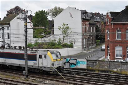 Charleroi, Mai 2024: Ein Lenkdrachen ist auf eine weiße Hauswand aufgemalt. Ein Gedenkgarten hinter Bahngleisen soll an die schrecklichen Taten im „Haus des Schreckens“ erinnern. An der Stelle stand eines der beiden Häuser, in denen Dutroux seine Verbrechen beging.
