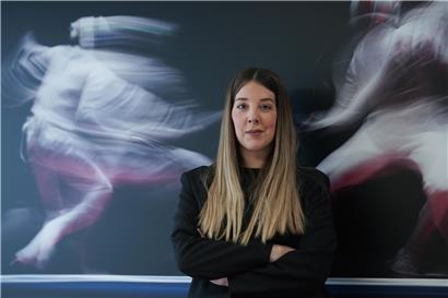 Christelle Diederich, Präsidentin von Sportspress.lu, spricht auf einer Pressekonferenz mit Mikrofon und Hintergrundlogo