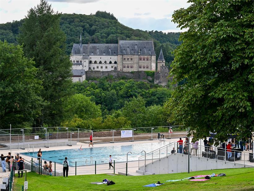 Freibad in Vianden mit Schwimmern und Blick auf das historische Schloss bei sonnigem Wetter