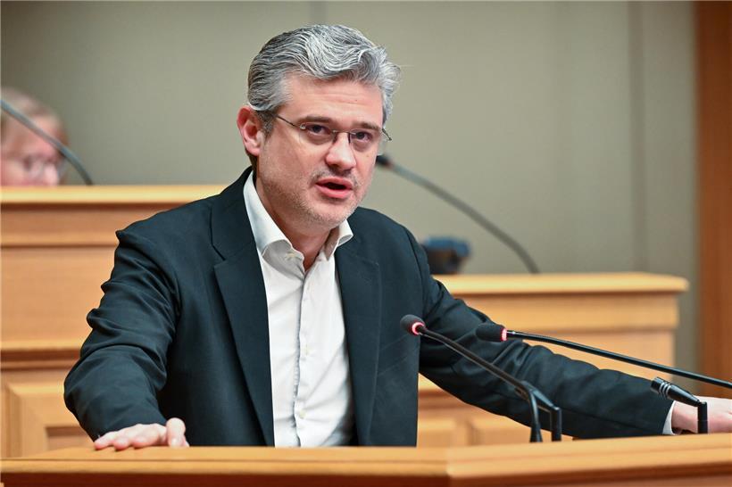 David Wagner von déi Lénk bei einer Rede vor rotem Hintergrund mit Parteilogos