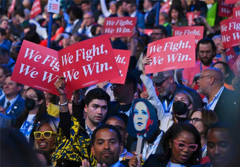 Delegierte halten Schilder mit der Aufschrift „We Fight, We Win“
