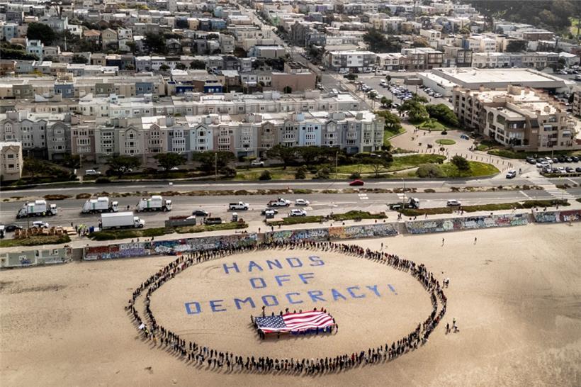 Demonstranten bilden am Ocean Beach einen menschlichen Kreis um eine US-Fölagge und den Slogan „Hands off democracy!" während eines Protestes gegen US-Präsident Trump. Die Demonstration ist Teil der landesweiten „Hände weg“-Kundgebungen
