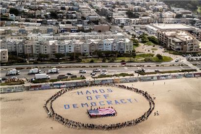 Demonstranten bilden am Ocean Beach einen menschlichen Kreis um eine US-Fölagge und den Slogan „Hands off democracy!" während eines Protestes gegen US-Präsident Trump. Die Demonstration ist Teil der landesweiten „Hände weg“-Kundgebungen
