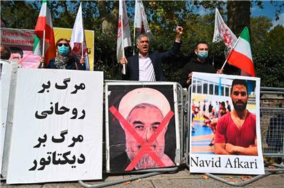 Demonstranten schwenken die Löwen- und Sonnenflagge des Nationalen Widerstandsrats des Iran und die weiße Fahne der Volksmudschaheddin des Iran, zweier iranischer Oppositionsgruppen, mit einem Plakat, das das durchgestrichene Gesicht des iranischen Präsidenten Hassan Rouhani zeigt, während sie am 12. September 2020 vor der iranischen Botschaft in London gegen die Hinrichtung des iranischen Ringer Navid Afkari…
