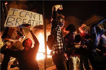 Demonstranten stehen mit einem Plakat mit der Aufschrift „I can’t breathe“ vor einem brennenden Gebäude des 3. Bezirks der Polizei von Minneapolis während der Proteste nach dem Tod von George Floyd, der infolge einer brutalen Festnahme durch einen Polizisten in Minneapolis starb. 
