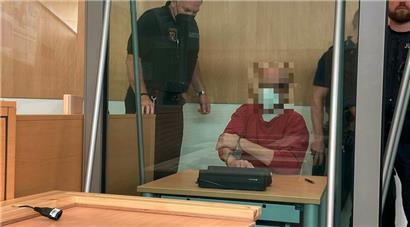 Der Angeklagte wird von Justizbediensteten zu seinem mit Panzerglas gesicherten Platz im Landgericht geführt
