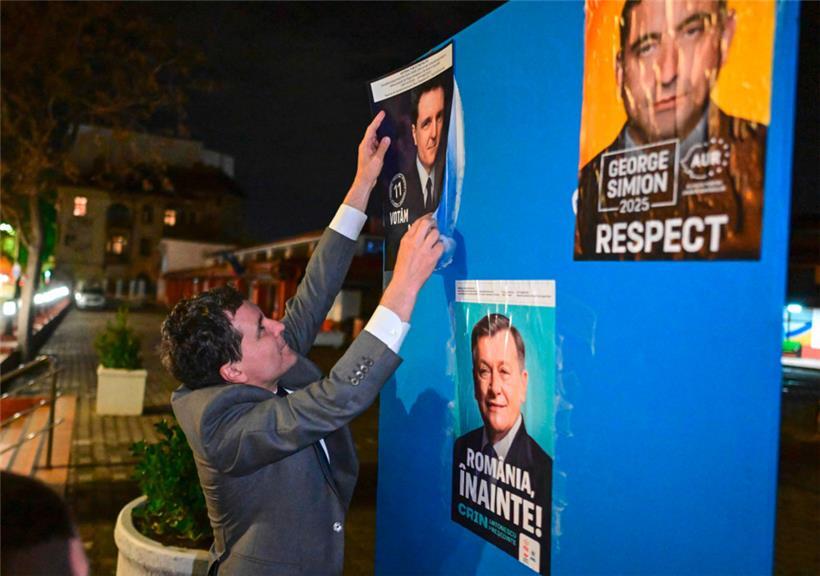 Der Bürgermeister von Bukarest und Präsidentschaftskandidat Nicusor Dan klebt ein Wahlplakat neben jene der Mitbewerber George Simion und Crin Antonescu
