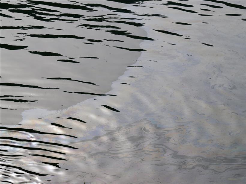 Ölfilm auf der Moseloberfläche bei sonnigem Wetter, sichtbare Umweltverschmutzung im Flusswasser