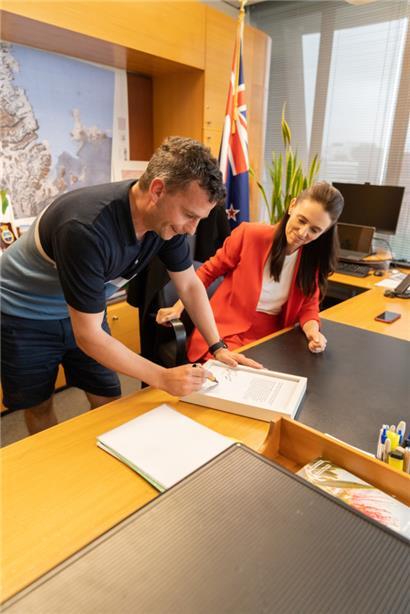 Der Oppositionsführer David Seymour und die neuseeländische Regierungschefin Jacinda Ardern unterzeichnen eine Kopie des Sitzungsprotokolls, in dem die Beleidigung festgehalten wurde, und die der Prostata-Krebs Stiftung rund 100.000 Neusseland-Dollar einbringt
