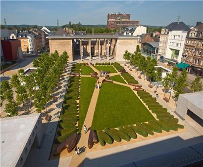 Der Platz in Richtung des „Musée national de la Résistance“. Fünf Wege, die die fünf Kontinente symbolisieren, laufen in der Mitte des Platzes zusammen. Künstlerisch geschnittene Hecken umgeben den zentralen Rasen. Im Hintergrund ist die „Centrale thermique“ der Arbed zu sehen, die 2017 abgerissen wurde.
