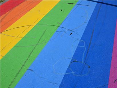 Der Regenbogen auf dem Radweg ist mit Reifenspuren übersät, die Umrisse eines Penis sind zu erkennen