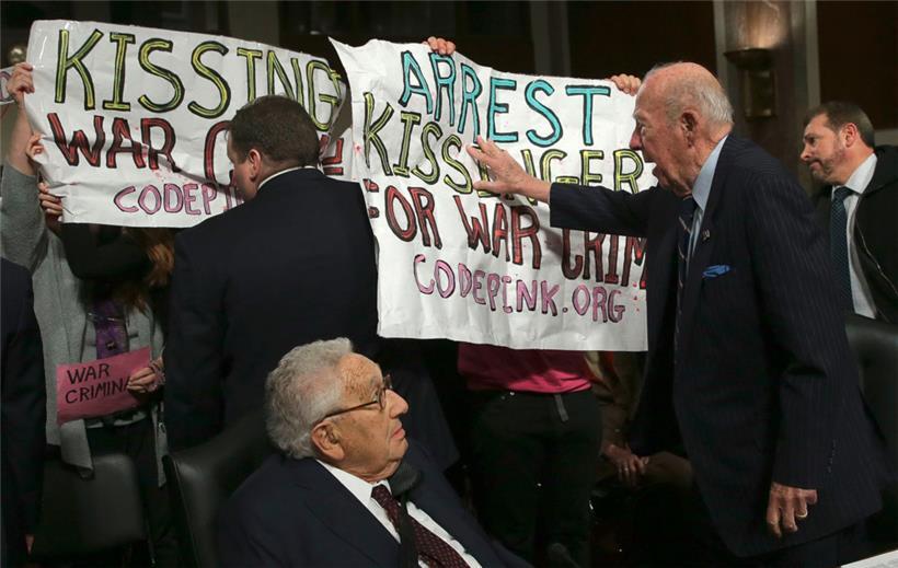 Der ehemalige US-Außenminister George Shultz (r) schiebt Demonstranten weg, die „Henry Kissinger für Kriegsverbrechen verhaften“ rufen, während der ehemalige US-Außenminister Henry Kissinger (l) zuschaut, bevor die beiden vor dem Senatsausschuss für Streitkräfte am 29. Januar 2015 in Washington, DC aussagen.
