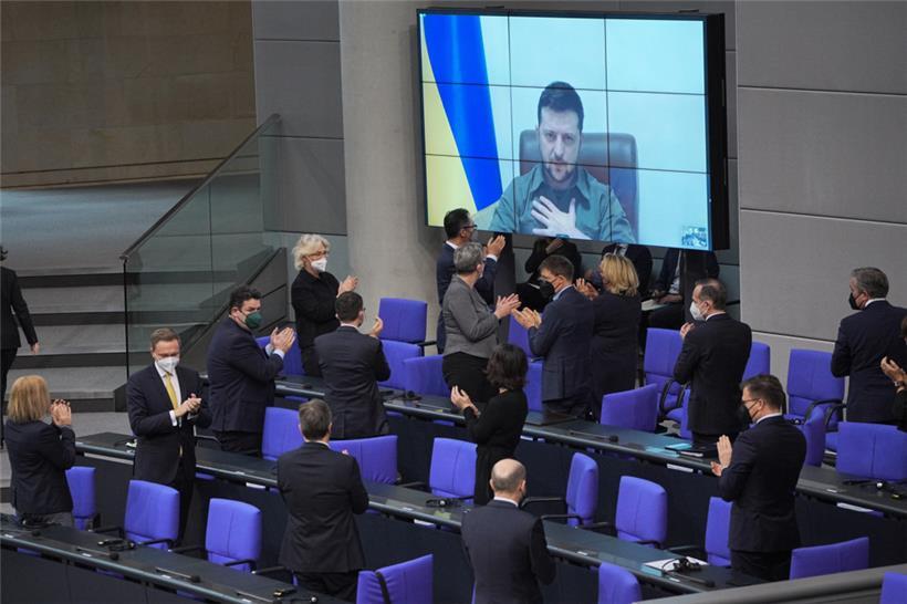 Der ukrainische Präsident Wolodymyr Selenskyj spricht auf einer Videoleinwand im Bundestag und bekommt Applaus von der Bundesregierung
