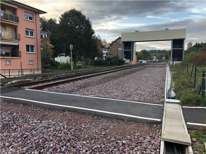 Der vorne im Bild zu sehende, erst kürzlich erneuerte ebene Fußgängerweg wird aus Sicherheitsgründen geschlossen. Im Hintergrund steht der jetzt errichtete, in Wellblech eingekleidete Fußgängerüberweg gleich neben dem Bahnhofsgebäude „Colmar-Usines“.

