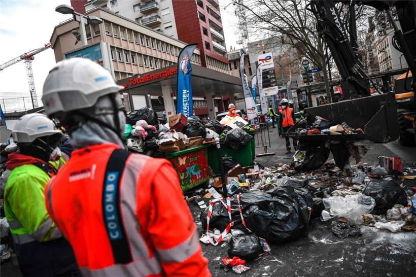 Des employés municipaux utilisent une pelleteuse mobile pour ramasser les ordures sur un trottoir à Paris
