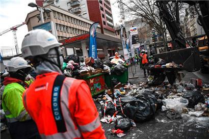Des employés municipaux utilisent une pelleteuse mobile pour ramasser les ordures sur un trottoir à Paris
