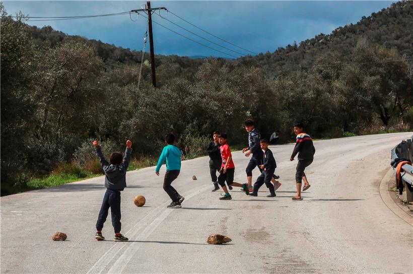 Des enfants du camp de réfugiés Moria jouent au football sur une route près du camp 

