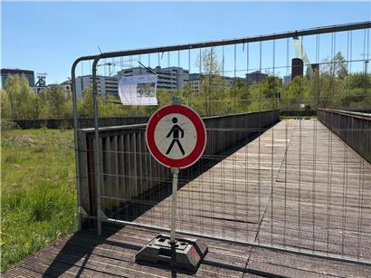 Gesperrte Holzbrücken am Weg zum Belval Park mit Absperrungen und Baustellenschildern im Grünen
