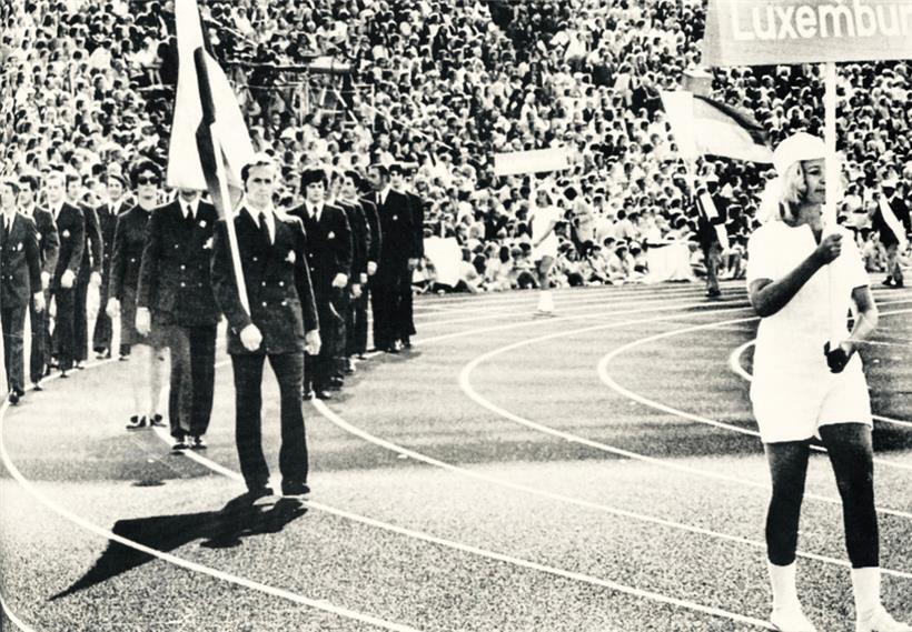 Die Luxemburger Delegation beim Einmarsch ins Olympiastadion von München am 25. August 1972. Hinter Fahnenträger Charles Sowa „Chef de mission“ Ferd Wirtz  (verdeckt) und die Bogenschützin Nelly Wies (mit Sonnenbrille).
