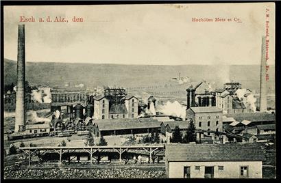 Die Metzeschmelz um 1900. Im Vordergrund sieht man die mit Eisenerz gefüllten Buggys, die vom Lallingerberg kommen und über Brücken zu den Hochöfen geführt werden; dahinter die Gleise, die die Fabrik versorgten. Die Reihe der Hochöfen mit Cowper, Schornsteinen und Gießhallen rundet das Bild ab. Hinter dem Werk rechts die Brauerei Buchholtz in Lallingen. Hinter…

